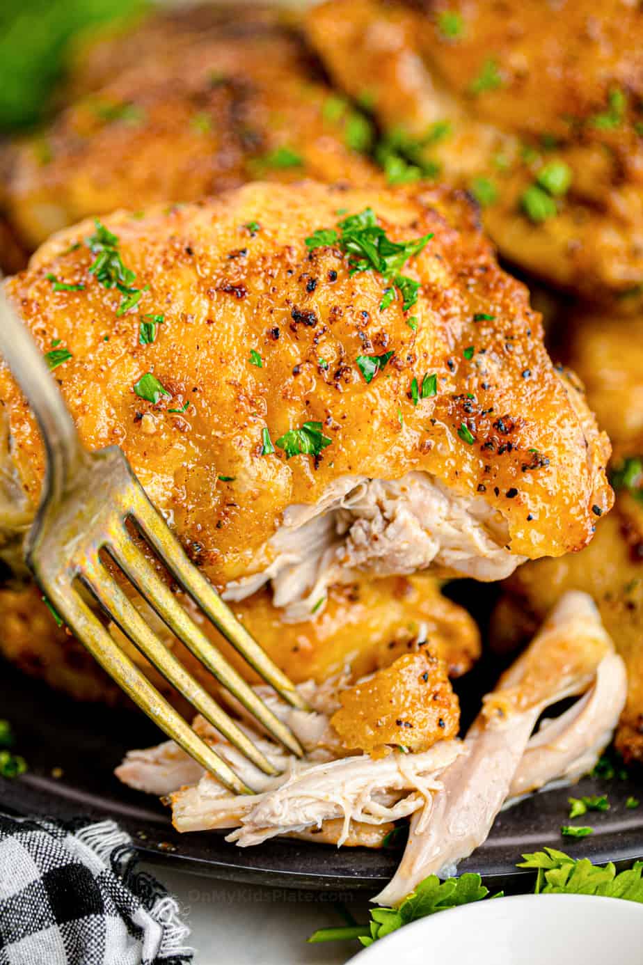 Close up of chicken thigh on a plate with a piece of chicken being pulled away with a fork.