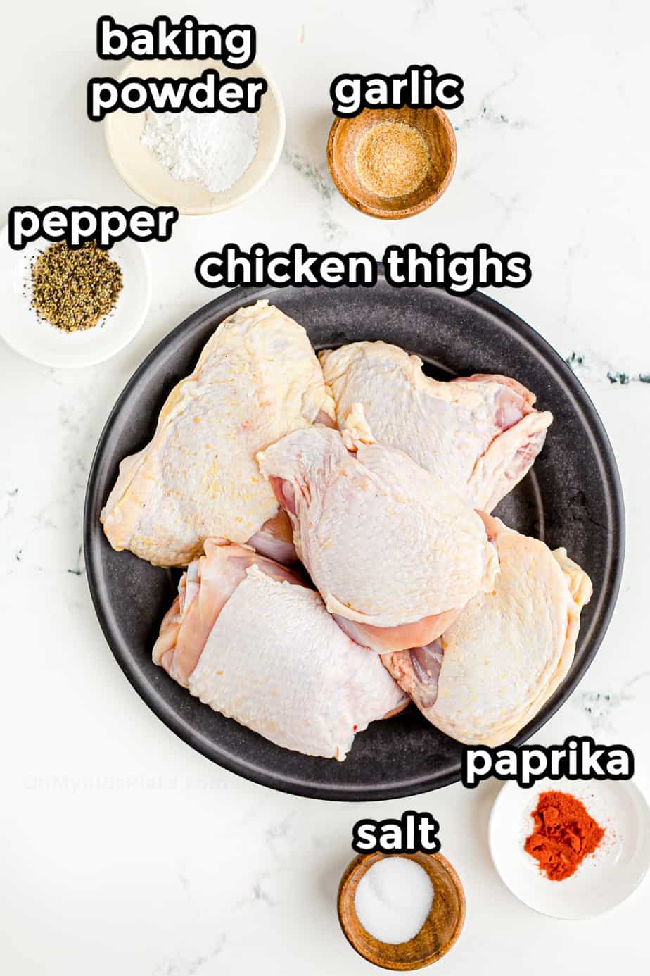 Ingredients for crispy chicken thighs in bowls from overhead with labels written on each bowl