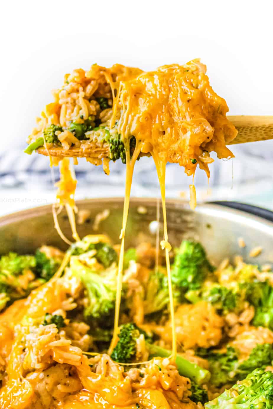 A scoop of cheesy rice mixed with chicken and broccoli being lifted from the pan as the cheese pulls.
