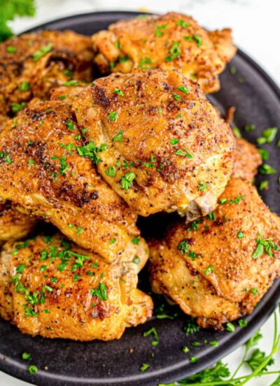 Chicken thighs on a black plate with herbs.