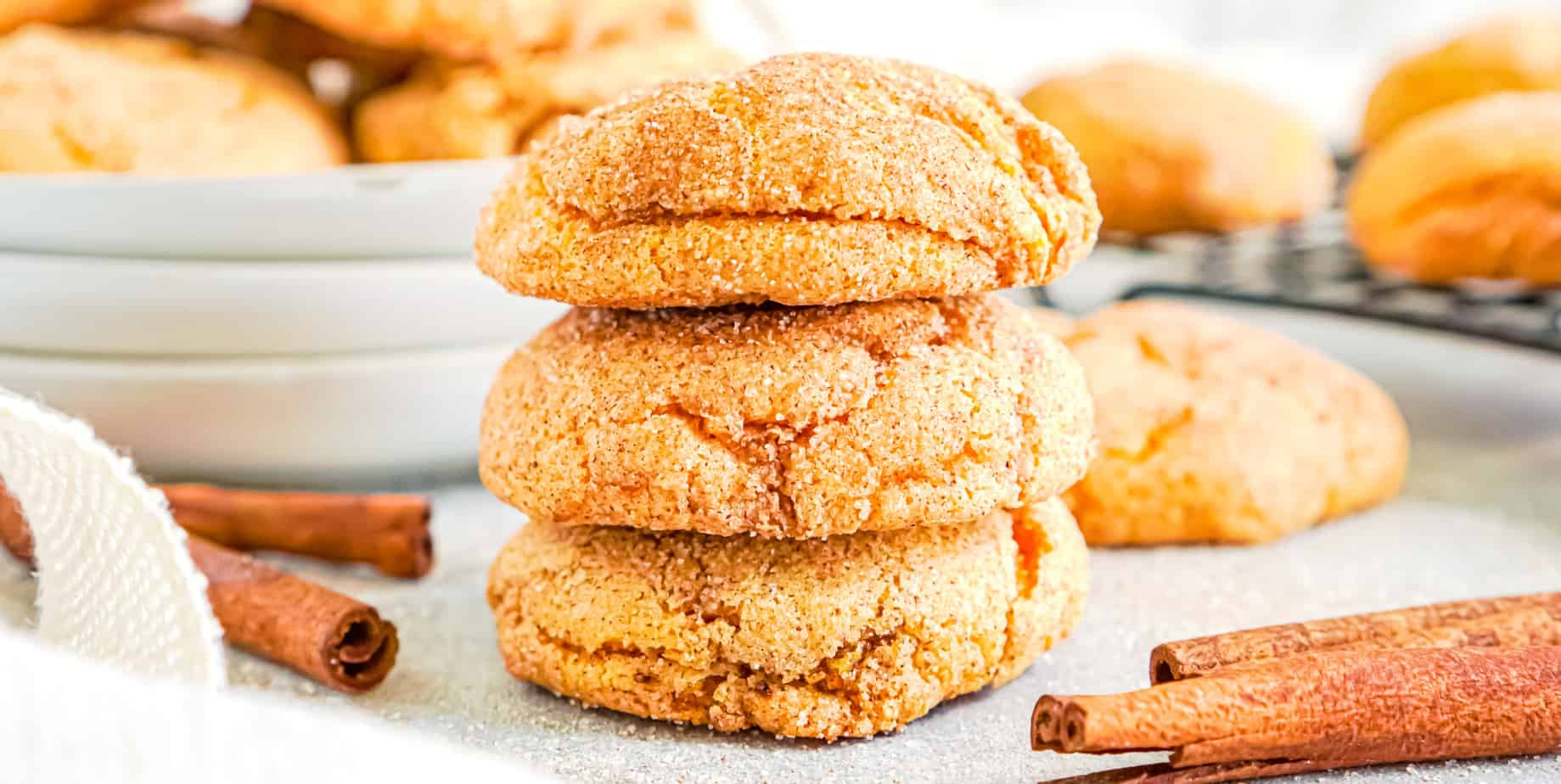 Wide view of pumpkin snickerdoodle cookies stacked up in a stack with more in the background