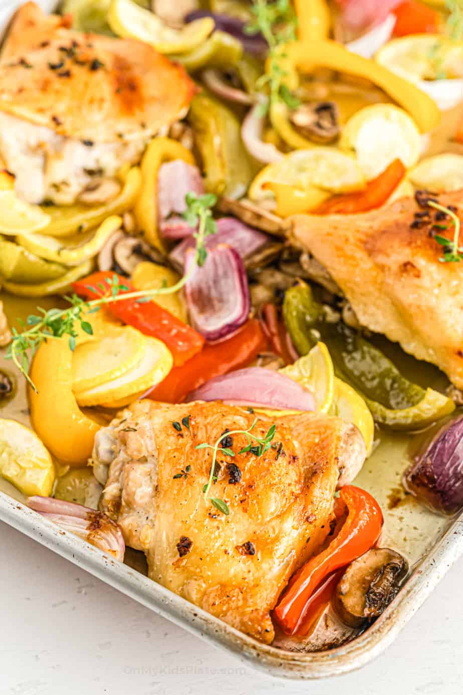 Oven baked chicken thighs with roasted vegetables close up on the corner of the pan.