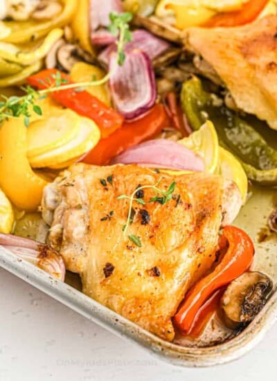 Baked chicken thighs and vegetables close up on the corner of the pan