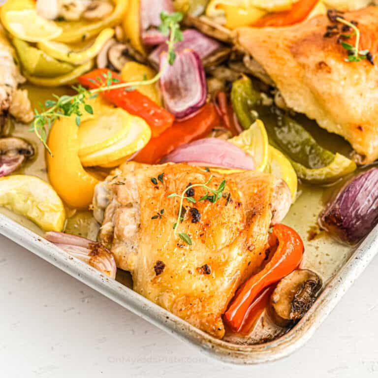 Baked chicken thighs and vegetables close up on the corner of the pan