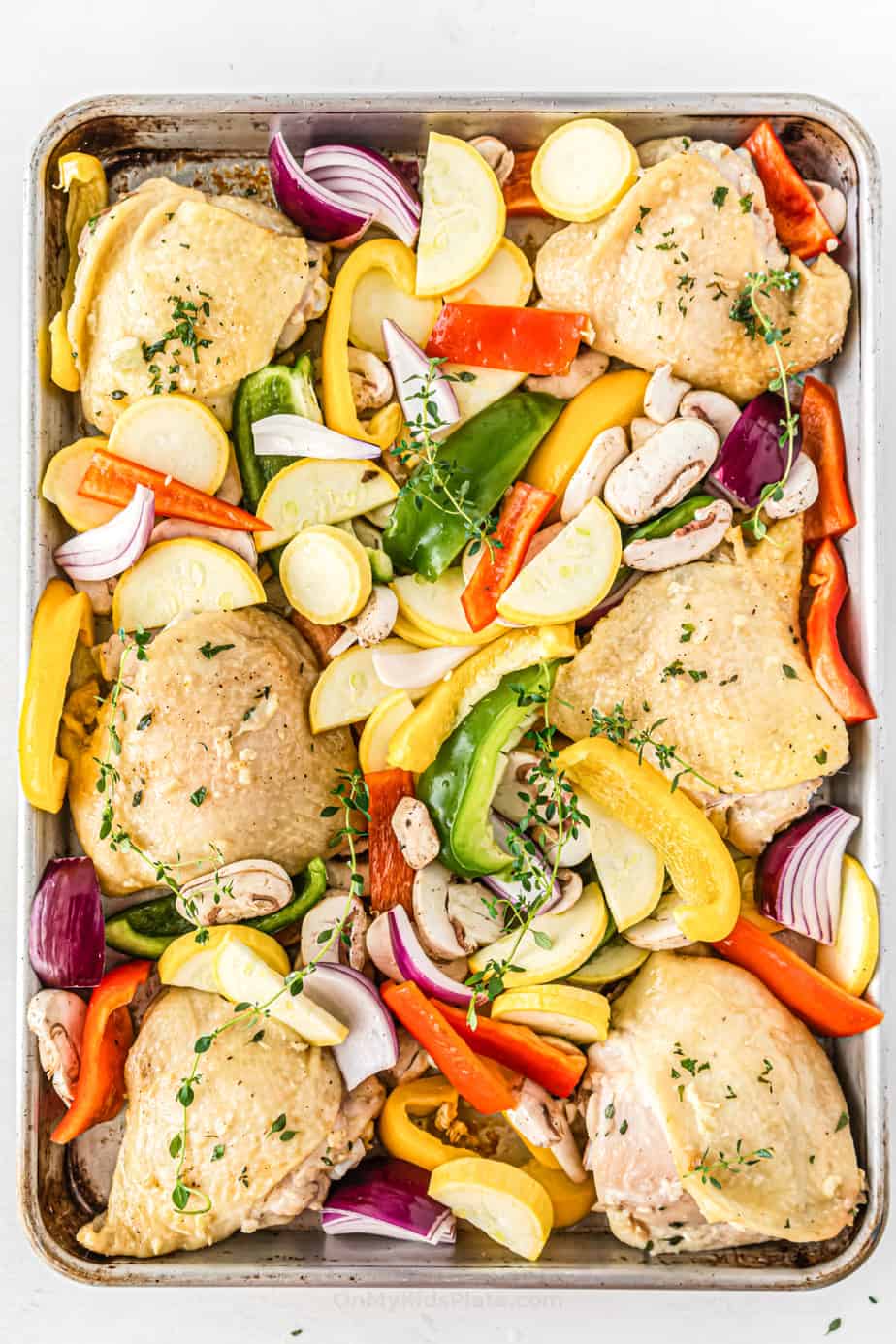 Half cooked chicken thighs on pan with squash, peppers and other vegetables  around them