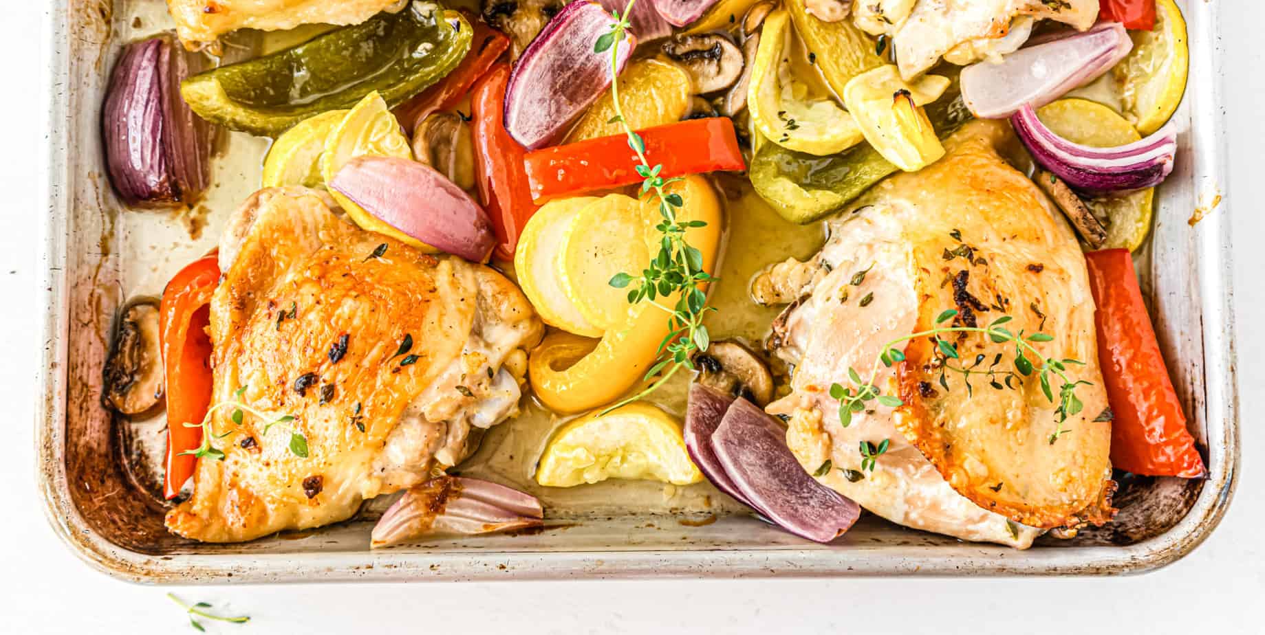 Baked chicken thighs with peppers, onions, squash and mushrooms on a sheet pan.