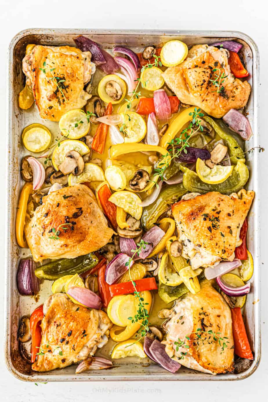 Golden brown chicken thighs with vegetables on a baking sheet.