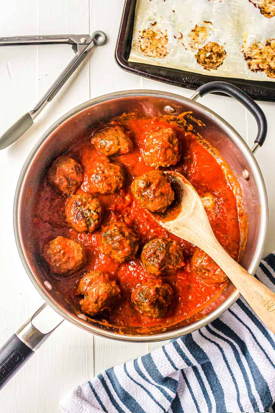 Meatballs in a pan in pasta sauce being stirred with a spatula