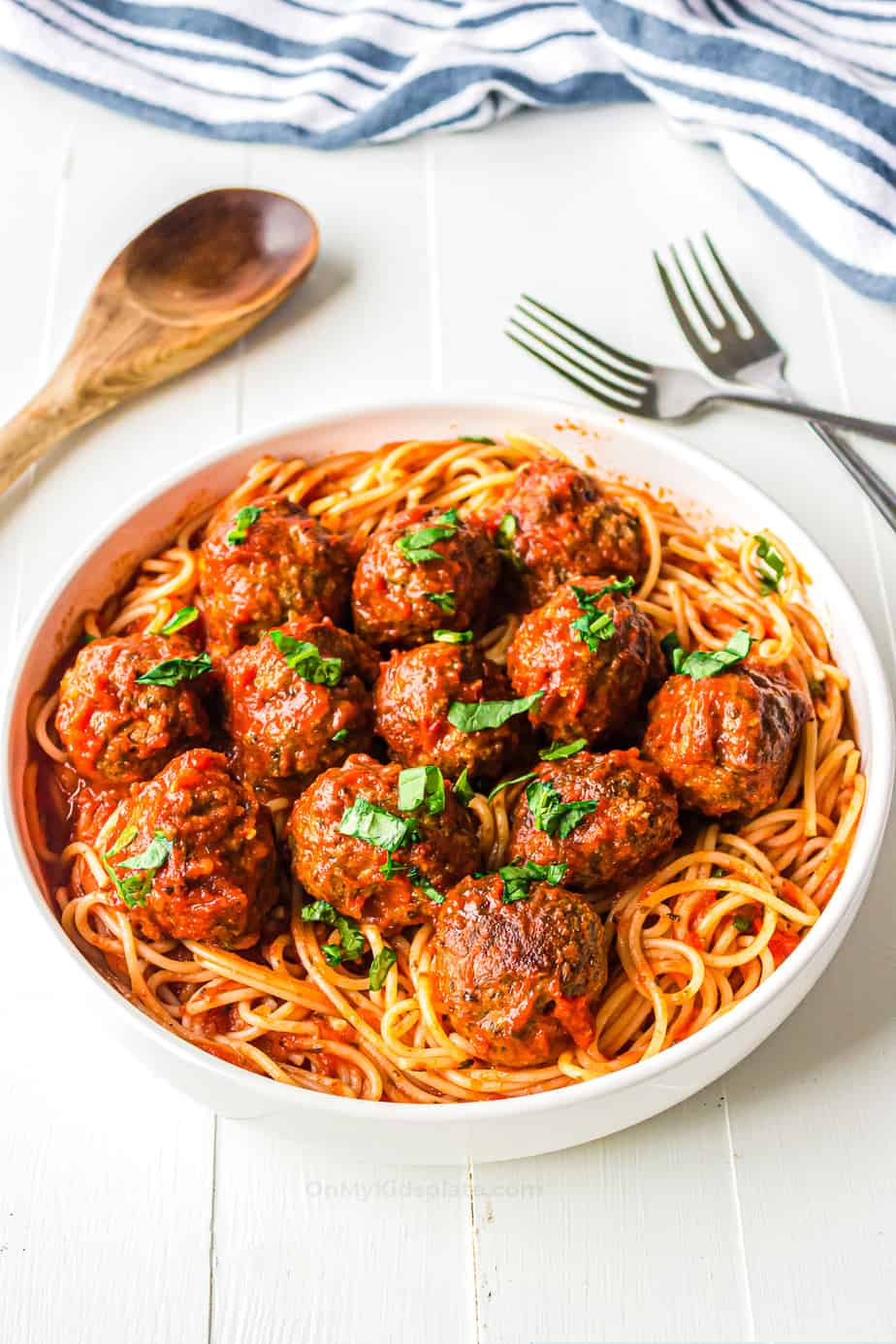 Meatballs in a large bowl over top of spaghetti with marinara sauce.