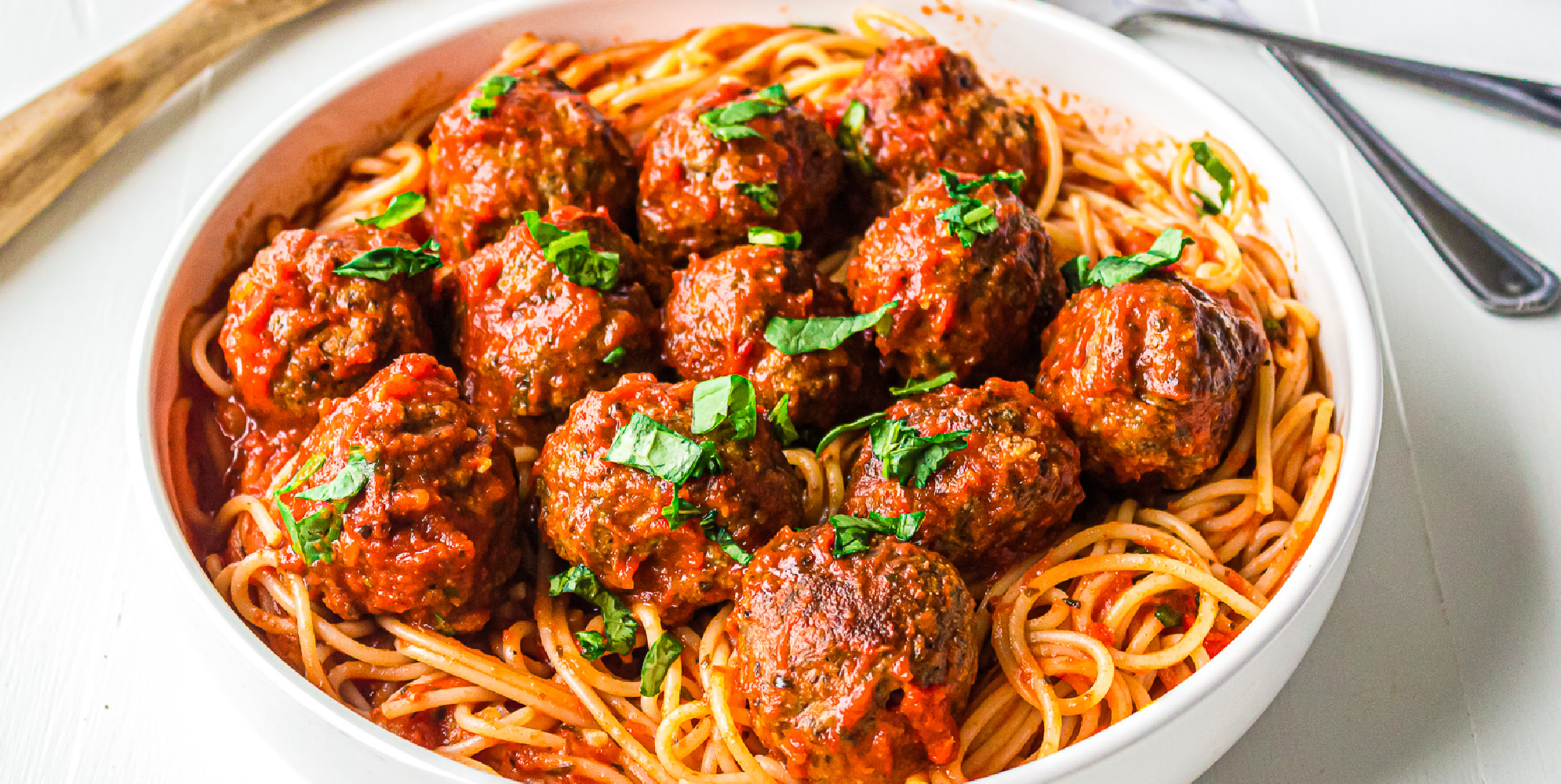 Wide shot of beef meatballs in tomato sauce on top of spaghetti in a bowl