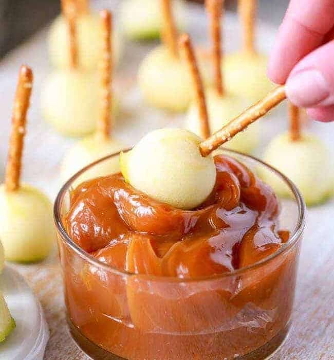 Mini apple pieces on pretzels being dipped in caramel
