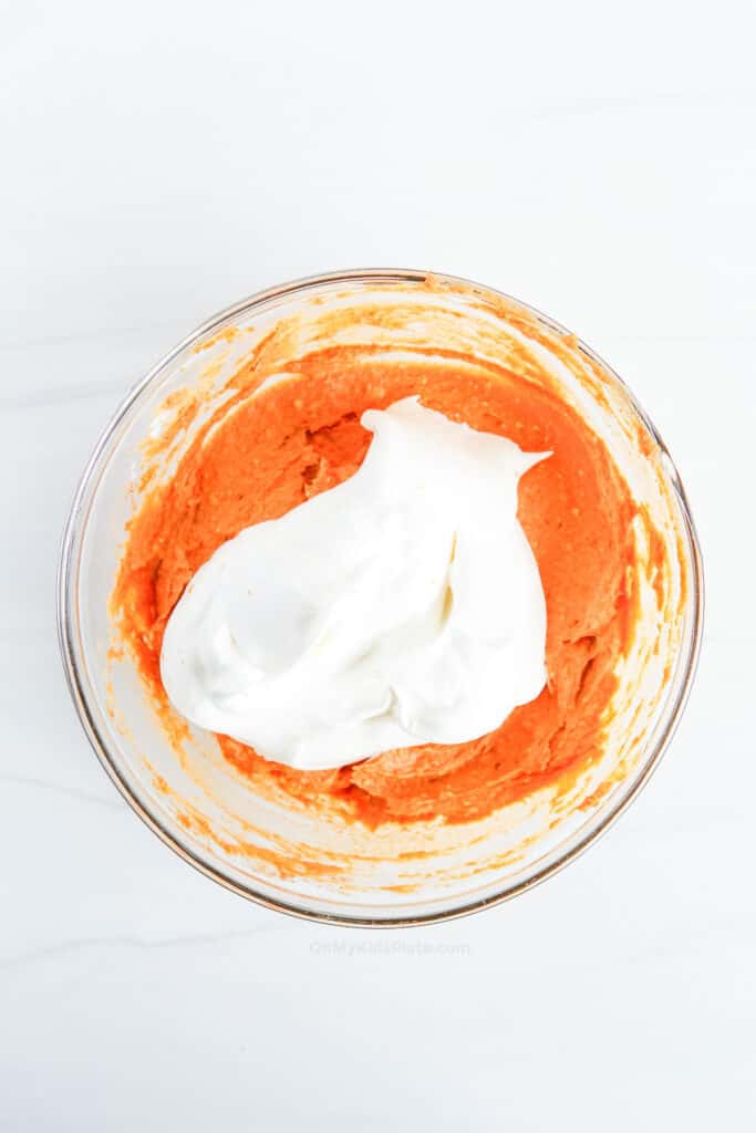Pumpkin pie dip with whipped topping being folded in to make it fluffy in a bowl.