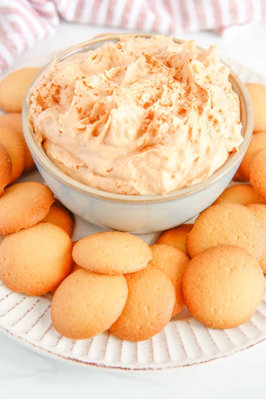Light orange creamy dip in a bowl on a plate surrounded by round cookies