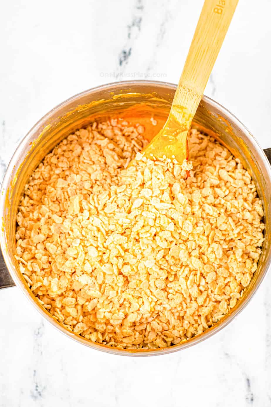 Adding Rice Krispie cereal to a pan on top of the pumpkin mixture.