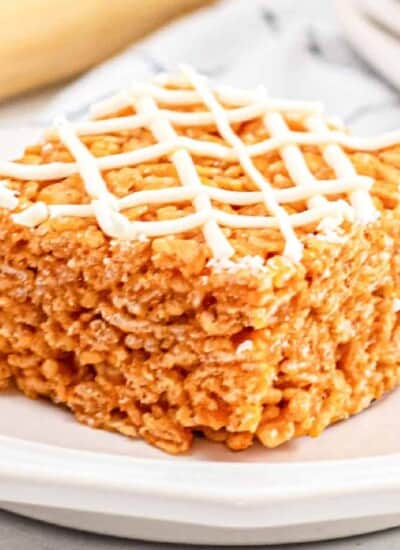 Orange pumpkin rice krispie treat at an angle on a plate close up topped with white chocolate