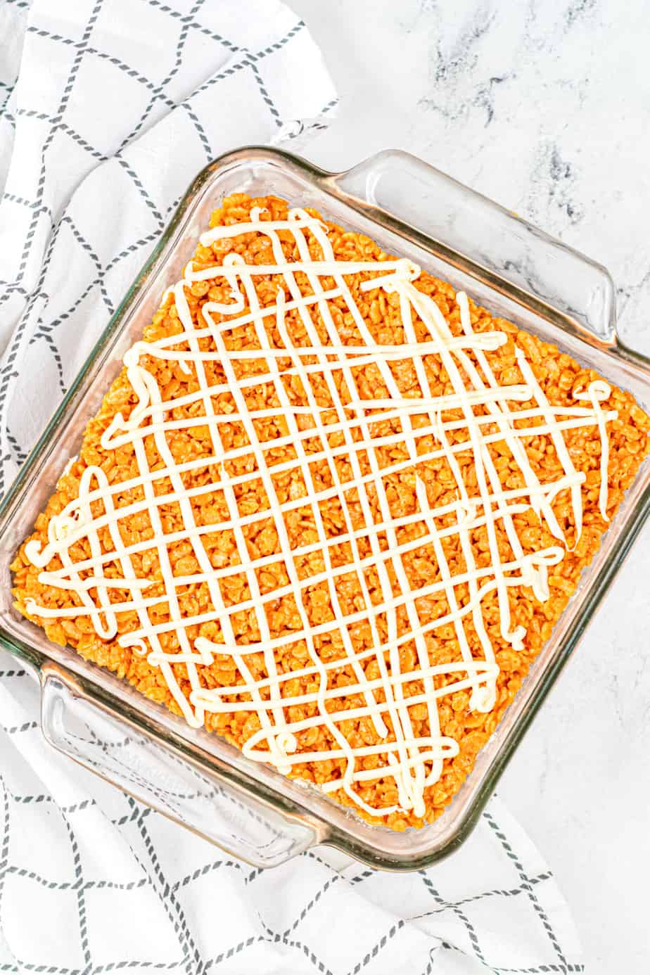 A square glass pan of pumpkin rice krispie treats drizzled with white chocolate.