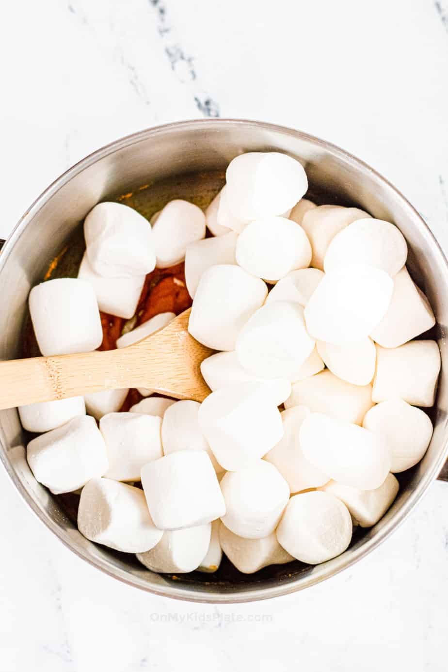 Adding marshmallows to a pan with a wooden spoon.