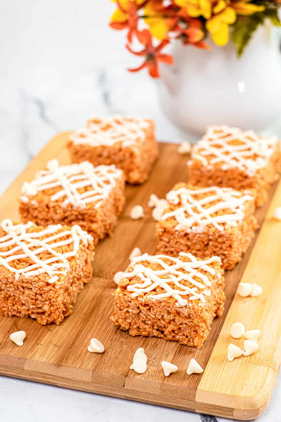 Pumpkin rice krispie treats sliced into squares on a cutting board with a white chocolate drizzle on top and white chocolate chips scattered on the cutting board.