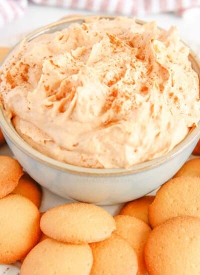 Close up of light orange pumpkin dip on a plate with vanilla cookies