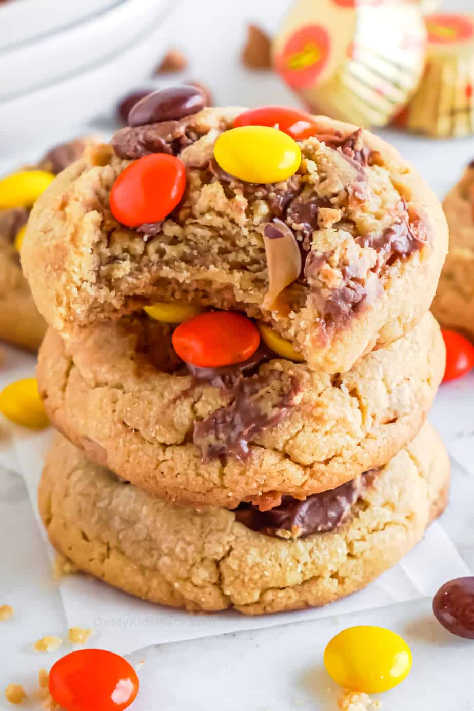Stack of cookies topped with Reese's pieces and peanut butter cup pieces. The top cookie has a bite missing