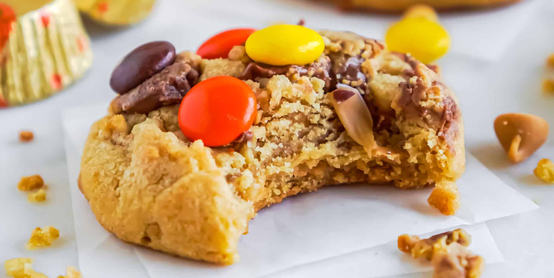 A close up of a cookie with Reese's Pieces and peanut butter with a bite taken out of it.