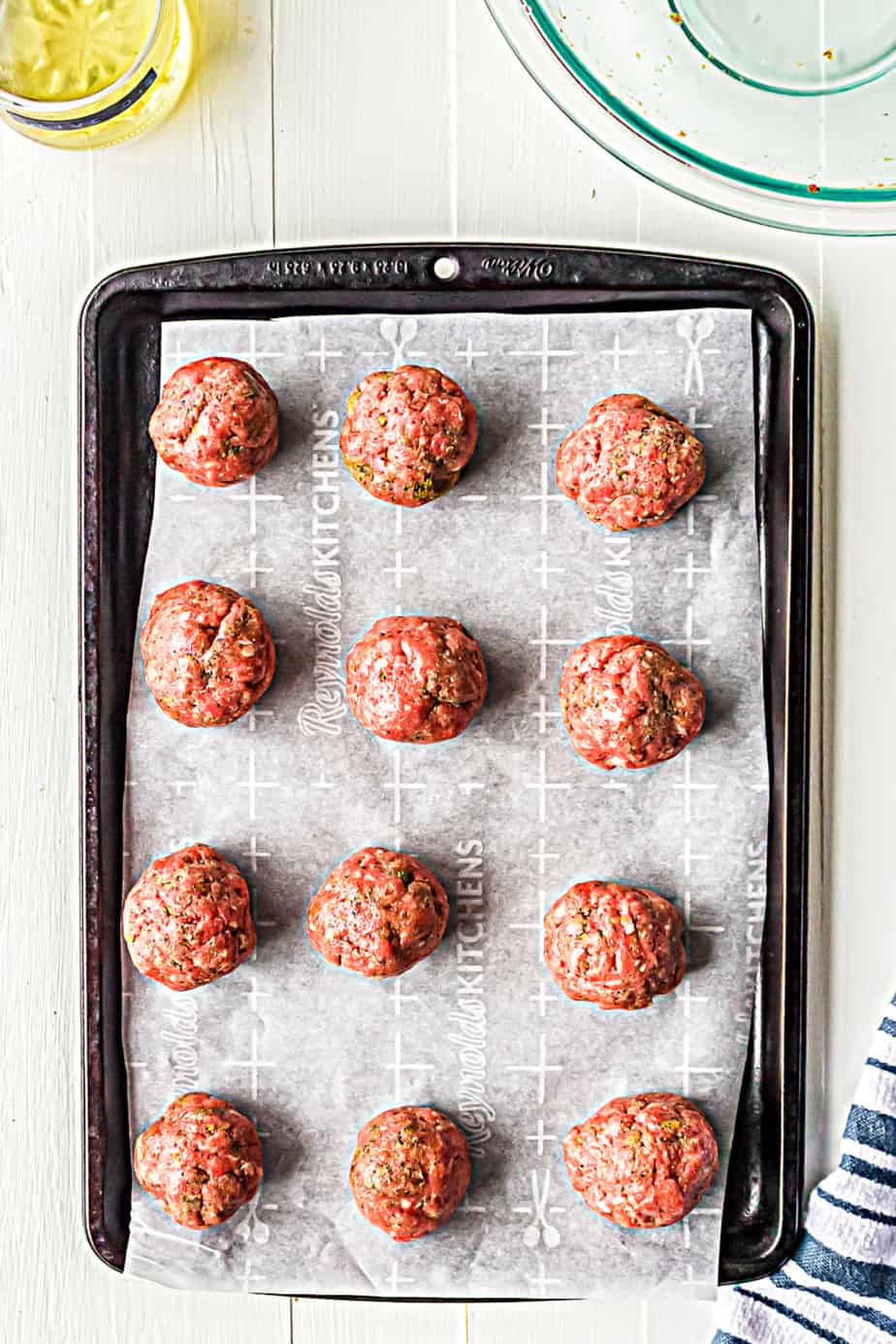 Overhead look at twelve raw meatballs on a baking pan lined with parchment paper.