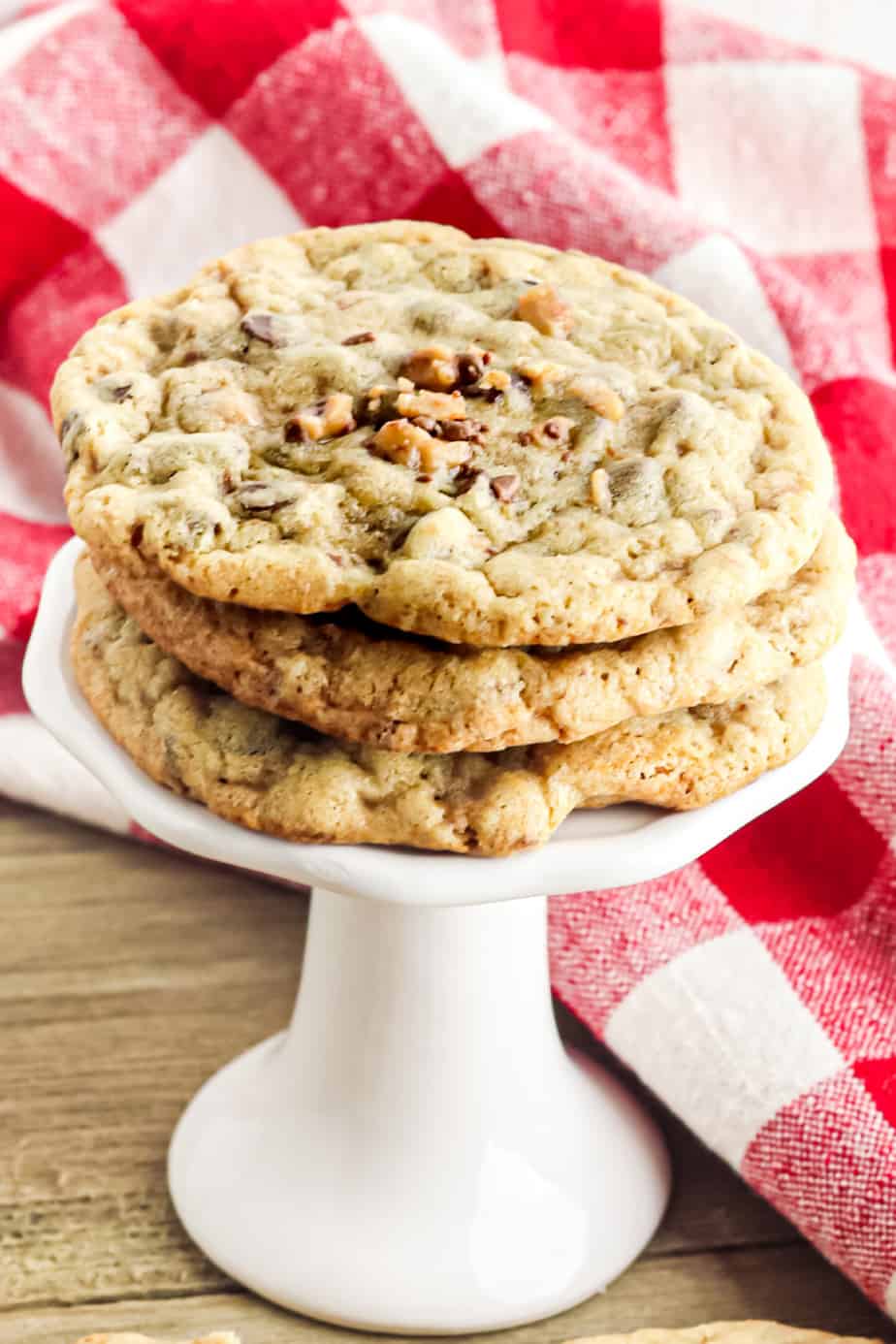 Stack of chocolate chip toffee cookies on a serving plate with a pedestal.