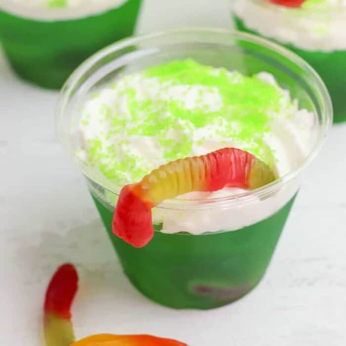 Green Jello cups decorated with whipped cream, sprinkles and gummy worms