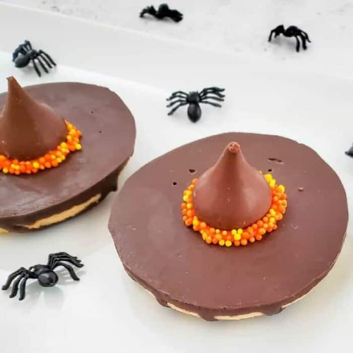A chocolate kiss candy on top of a cookie decorated to look like a witch hat.