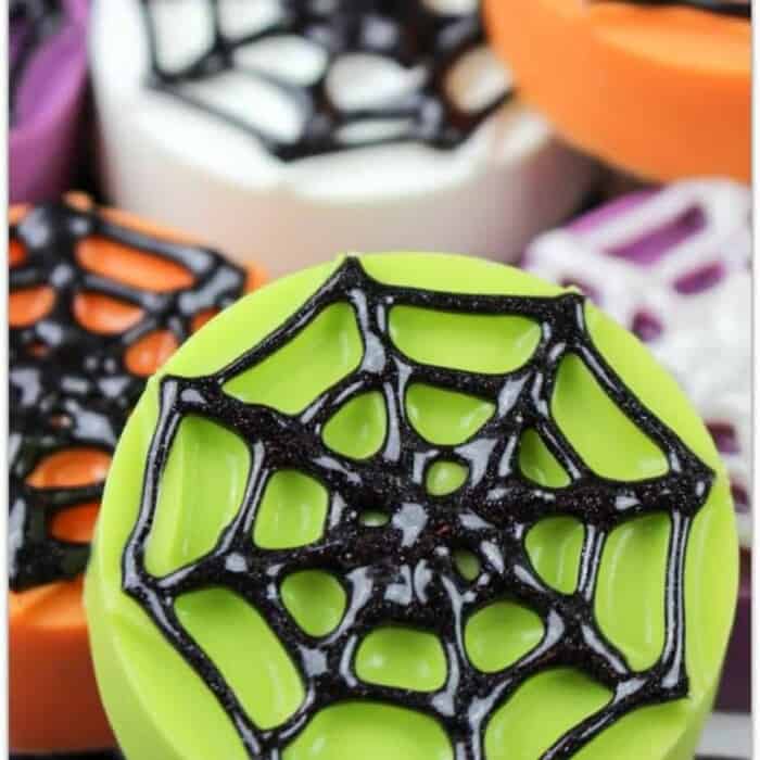 Oreos covered in green white and orange chocolate and decorated with candy spider webs
