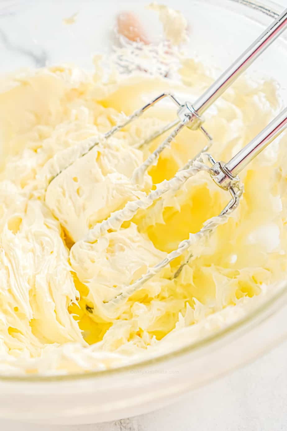 Butter and cream cheese being beaten with a hand mixer in a bowl close up