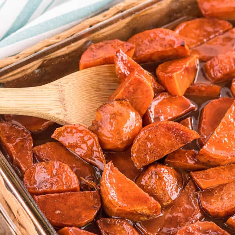 Close up candied yams in a pan with a wooden spoon scooping