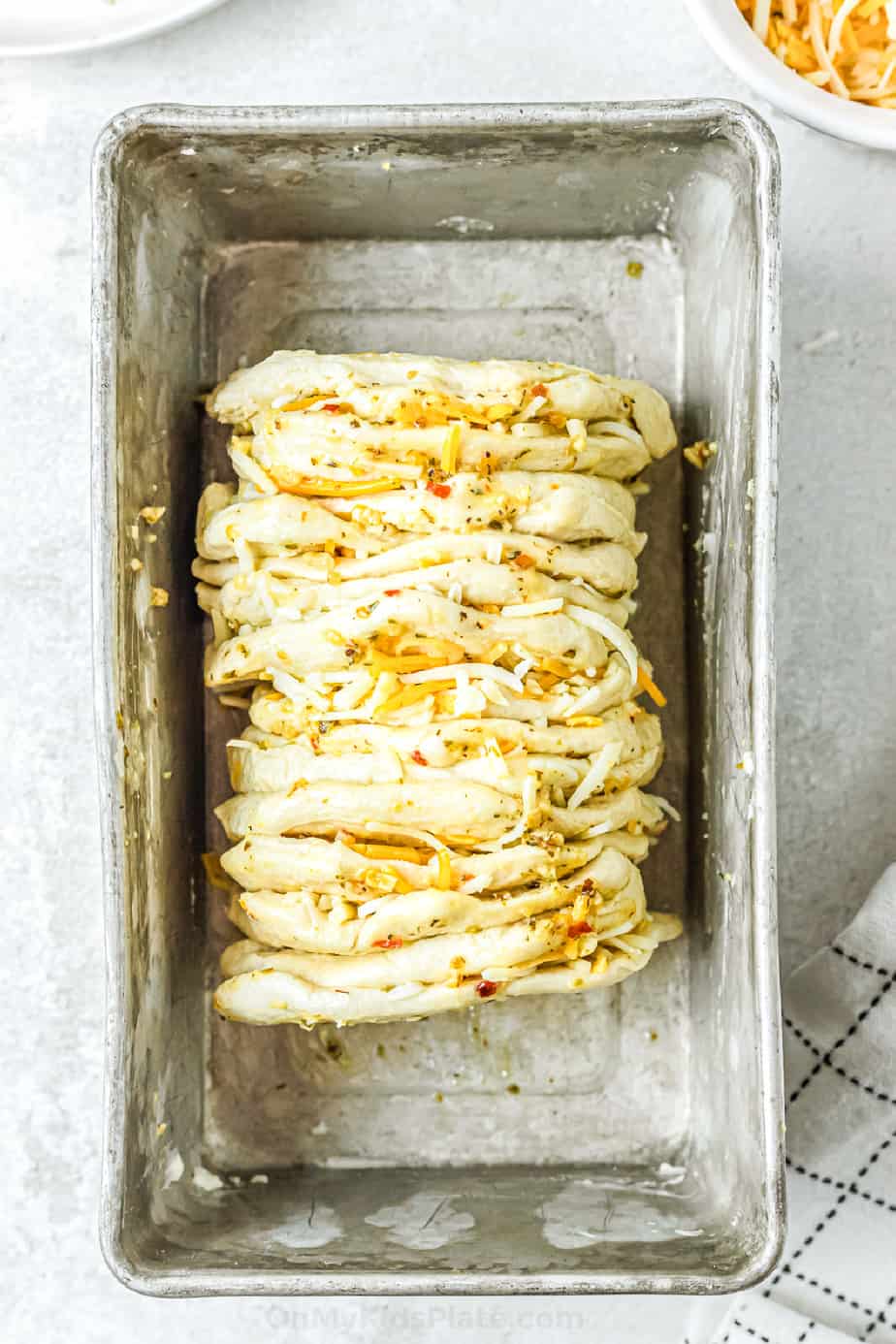 Biscuit dough layered with cheese and herbs stacked in a bread pan from overhead