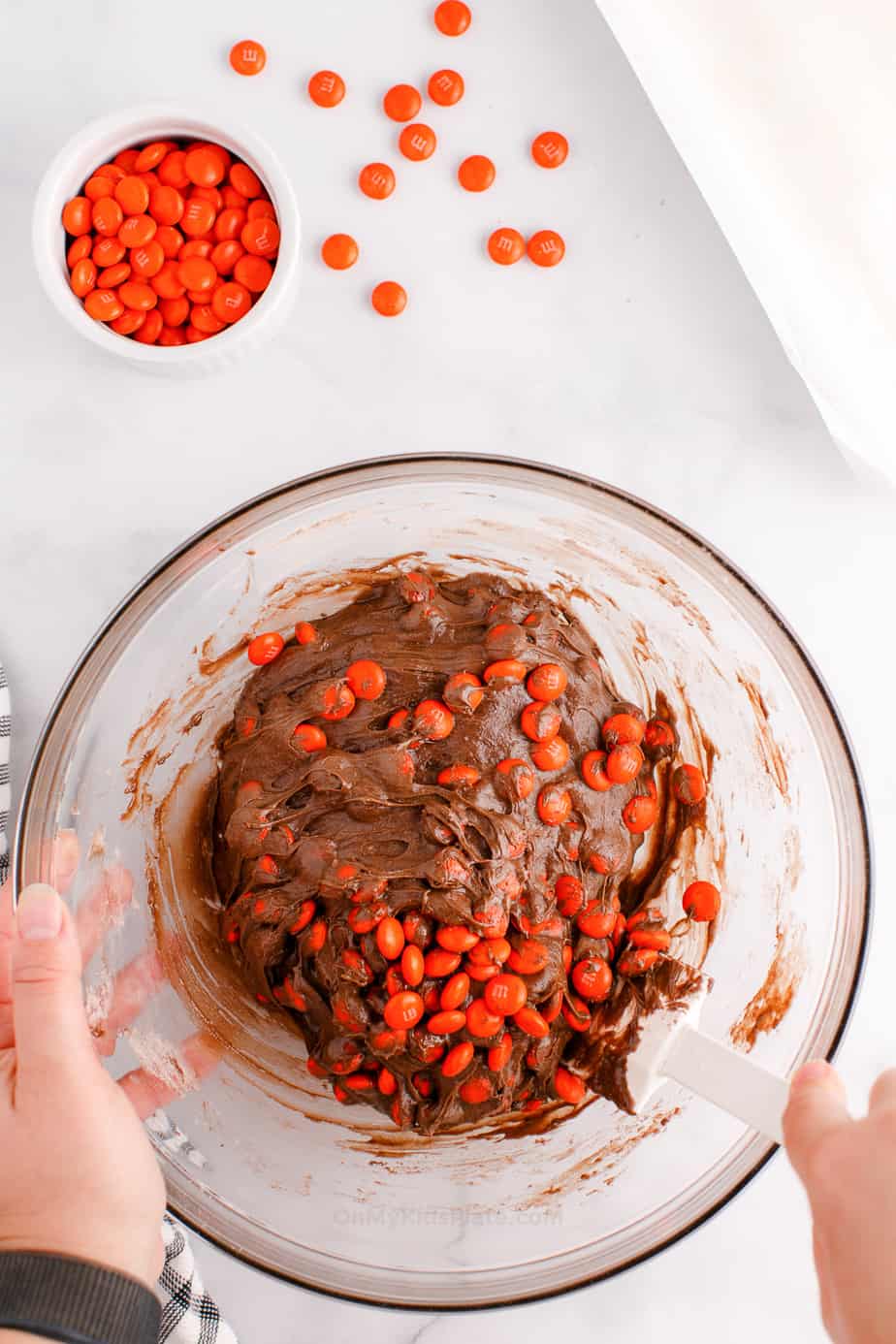 Orange candies being mixed into a cookie dough in a bowl from overhead
