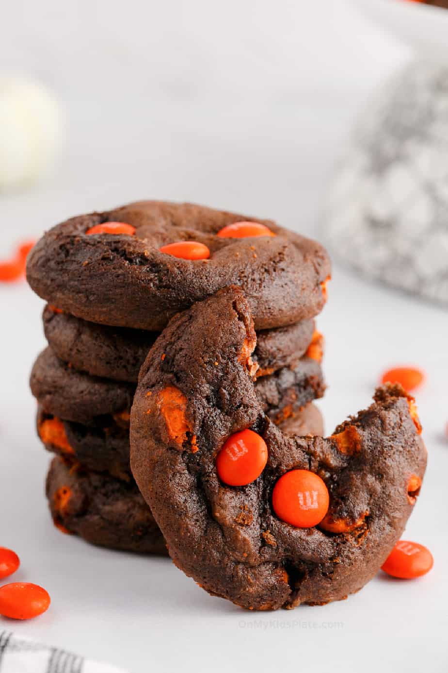 Stack of chocolate cookies with orange candies. One cookie has a bite missing