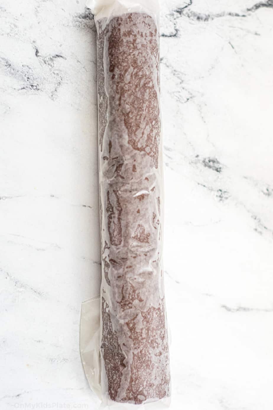 Chocolate cookie dough rolled into a long log and wrapped in parchment paper.