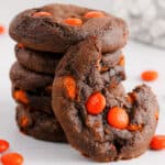 stack of chocolate cookies with orange candies, one cookie has a bite missing