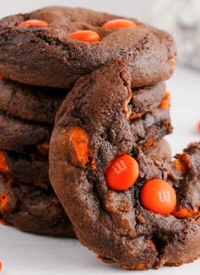 stack of chocolate cookies with orange candies, one cookie has a bite missing