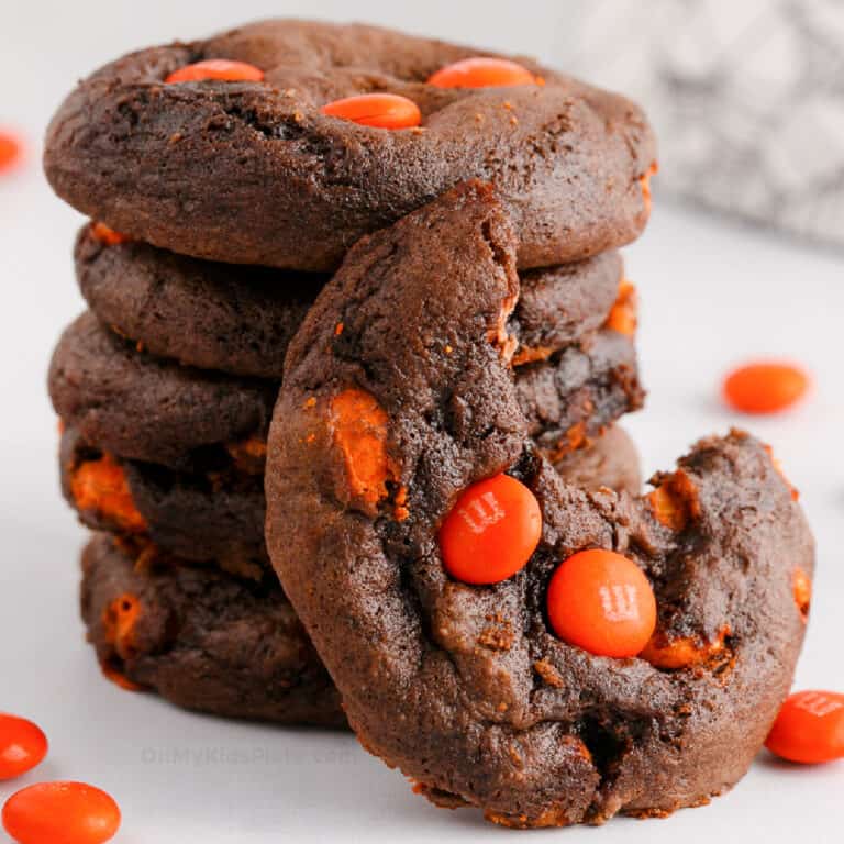 stack of chocolate cookies with orange candies, one cookie has a bite missing