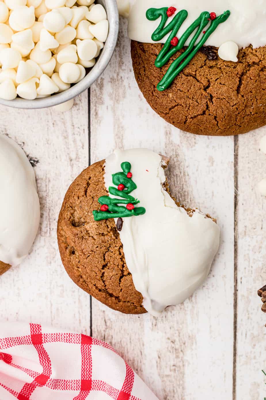 Close up of a molasses cookie dipped in white chocolate decorated with a Christmas tree with a bite missing.