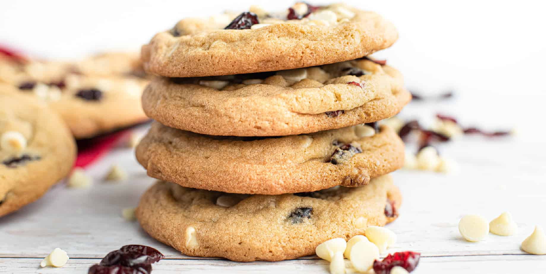 Cookies stacked up in a stack of four from the side with cranberries and white chocolate chips scattered around the base