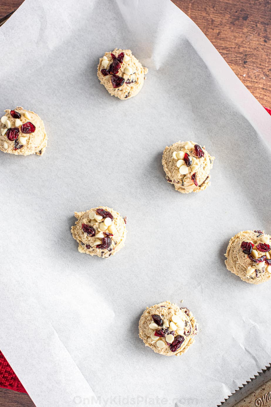 Raw cookie dough full of dried cranberries and white chocolate chips on a parchment lined baking pan zoomed in and tilted to the side.