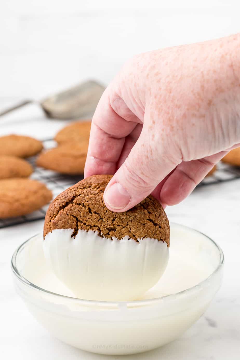 Hand dipping a molasses cookie in white chocolate from the side
