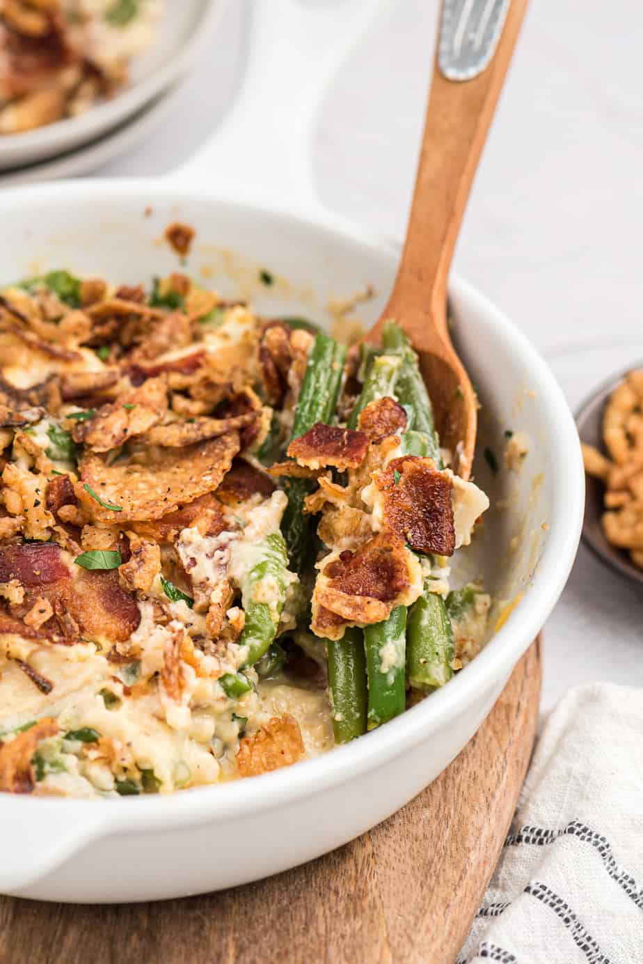 Side view of a spoon scooping green beans bacon and crispy onions in a white creamy sauce in a casserole dish.