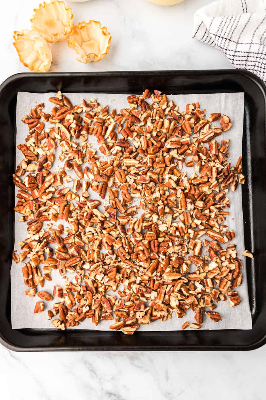 Chopped pecans on a baking pan lined with parchment paper