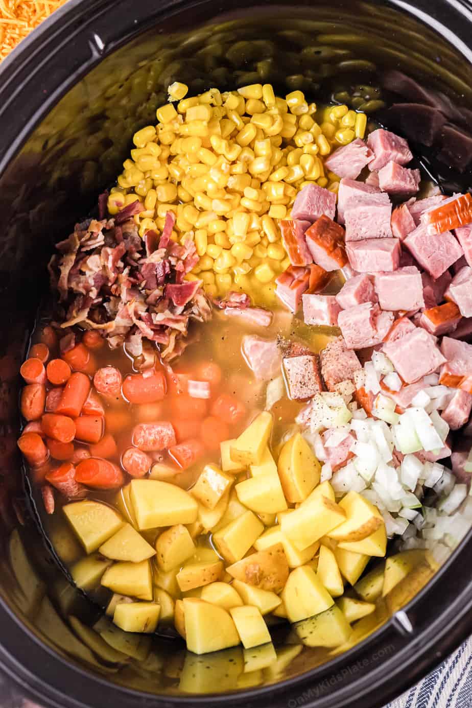 Diced potatoes, ham, bacon, carrots, onions and corn in a broth in a slowcooker pot.