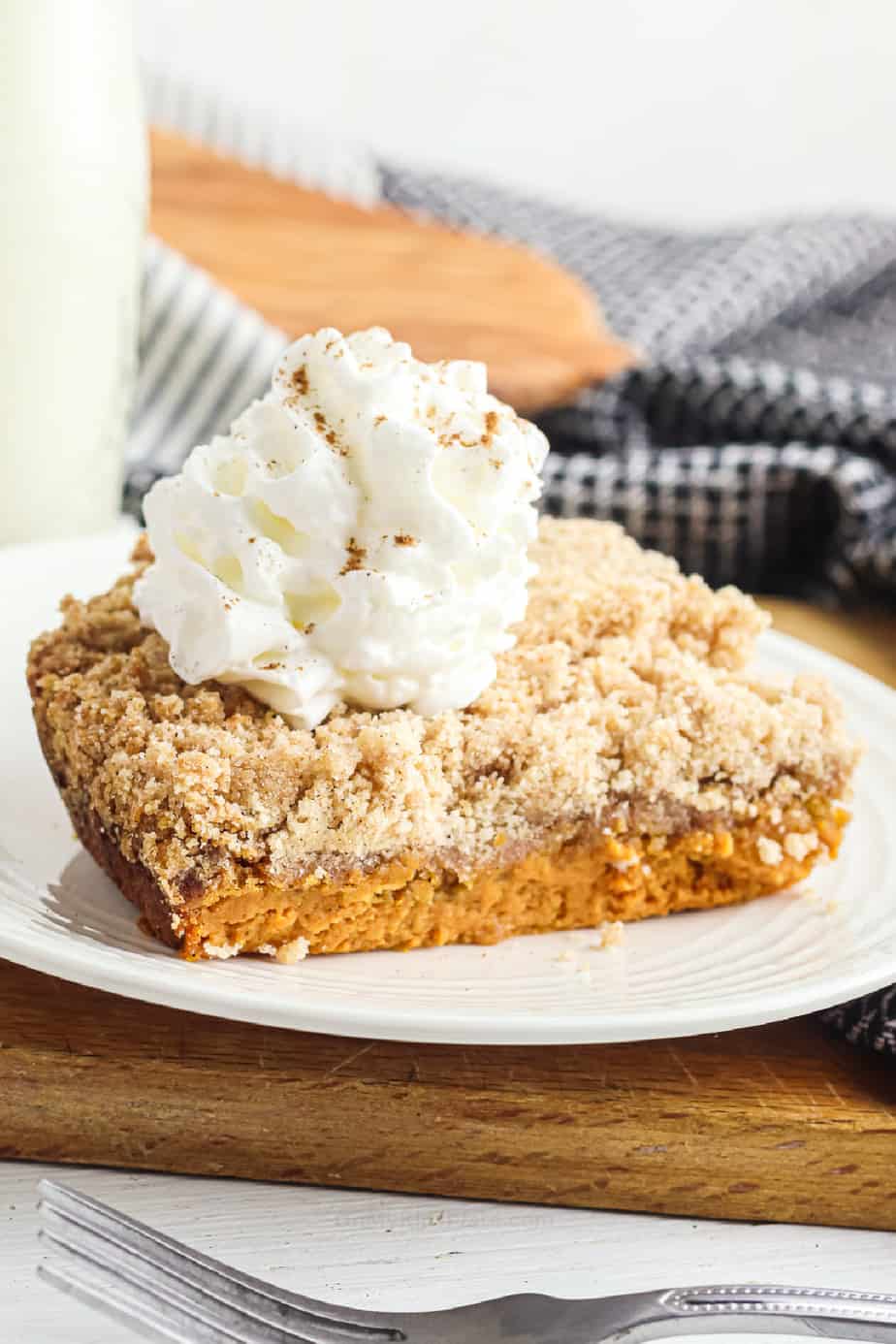 Slice of layered pumpkin dump cake toped with whipped cream on a plate form the side