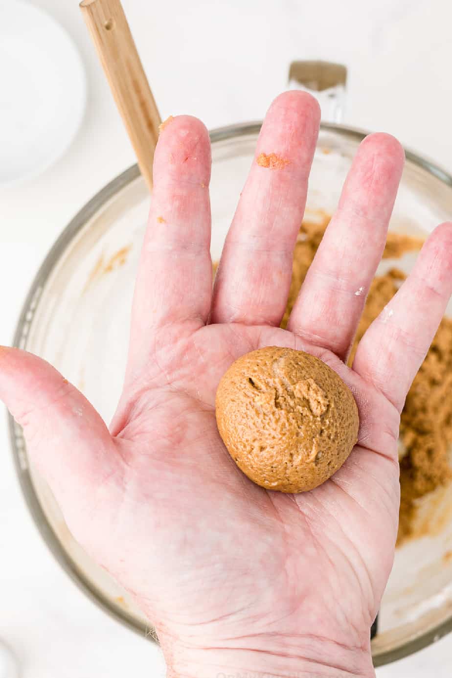 Hand holding ball of cookie dough after rolling over mixing bowl