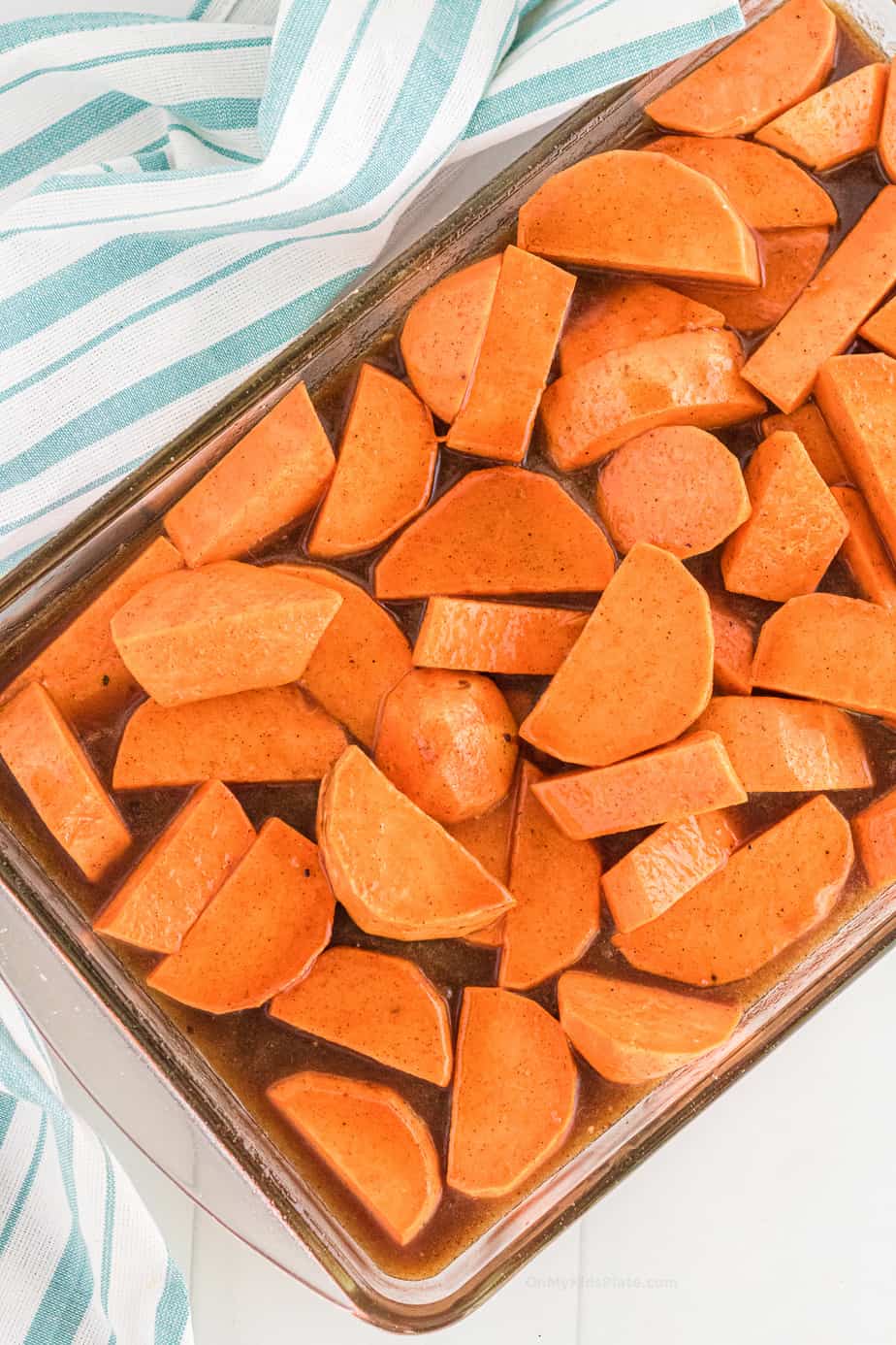 Sliced raw yams in a baking dish covered in brown sauce
