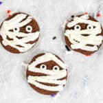 Three chocolate cookies close up decorated with frosting and candy eyes to look like mummies